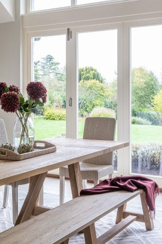 Large oak kitchen table with rattan chair and bench and views over the garden.