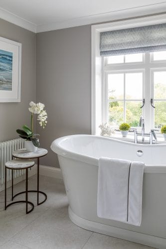 Large free standing bath with views over the garden. Antique bronze tables with a white orchid.