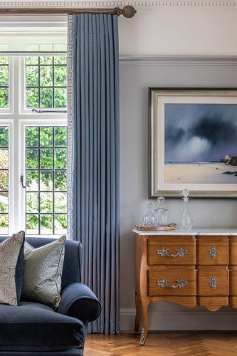 Blue wool full length curtains with dramatic blue landscape artwork and walnut chest of drawers with marble top.