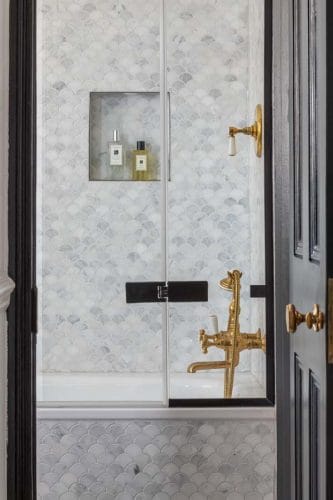 Marble scallop tiled bathroom with un lacquered brassware and black edged shower screen.
