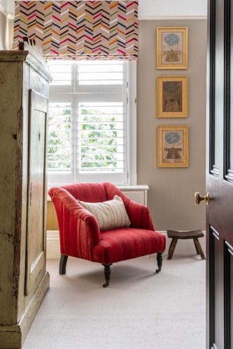 Red kilim upholstered armchair with antique Indian prints on the wall and antique Scandinavian wardrobe.