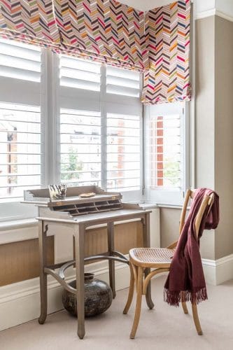 Small dressing table sitting in bay window with multi coloured zig zag stitched roman blinds.