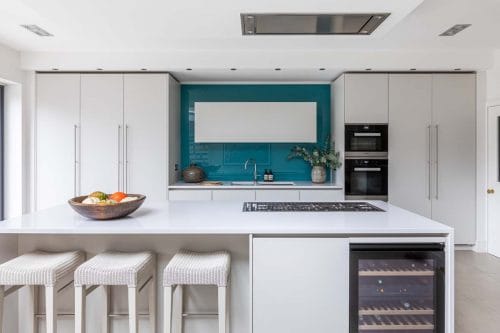 Contemporary white handleless kitchen with large island and turquoise splash back.